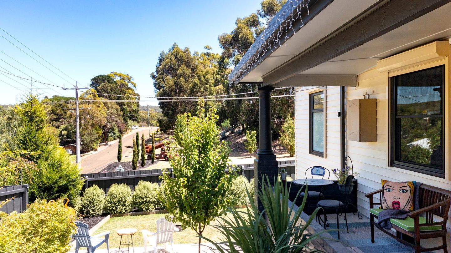 A patio with outdoor furniture, a view of the street, and a house with a large window.