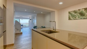 A modern kitchen with a central island, a dining area with chairs, and a staircase leading to an upper level. - Spacious apartment for 6 with terrace and WiFi · Llafranc (Llafranc)