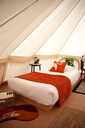 A tent with a bed, a small table with a lamp, and a chair.
