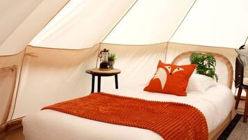 A tent with a bed, a small table with a lamp, and a chair.