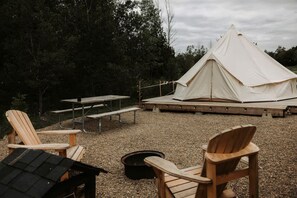 Zona de camping con carpas, una mesa de picnic y sillas de madera.