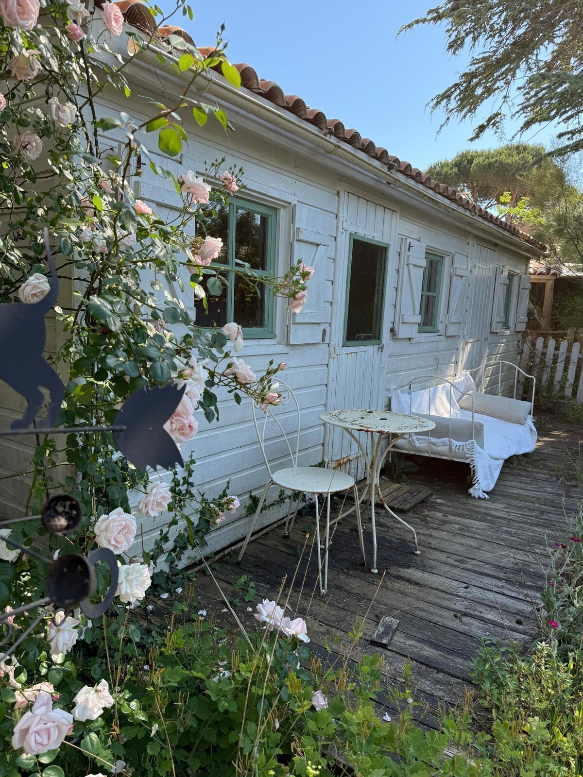 A rustic wooden house with a porch, a white outdoor seating area, and a garden with roses.