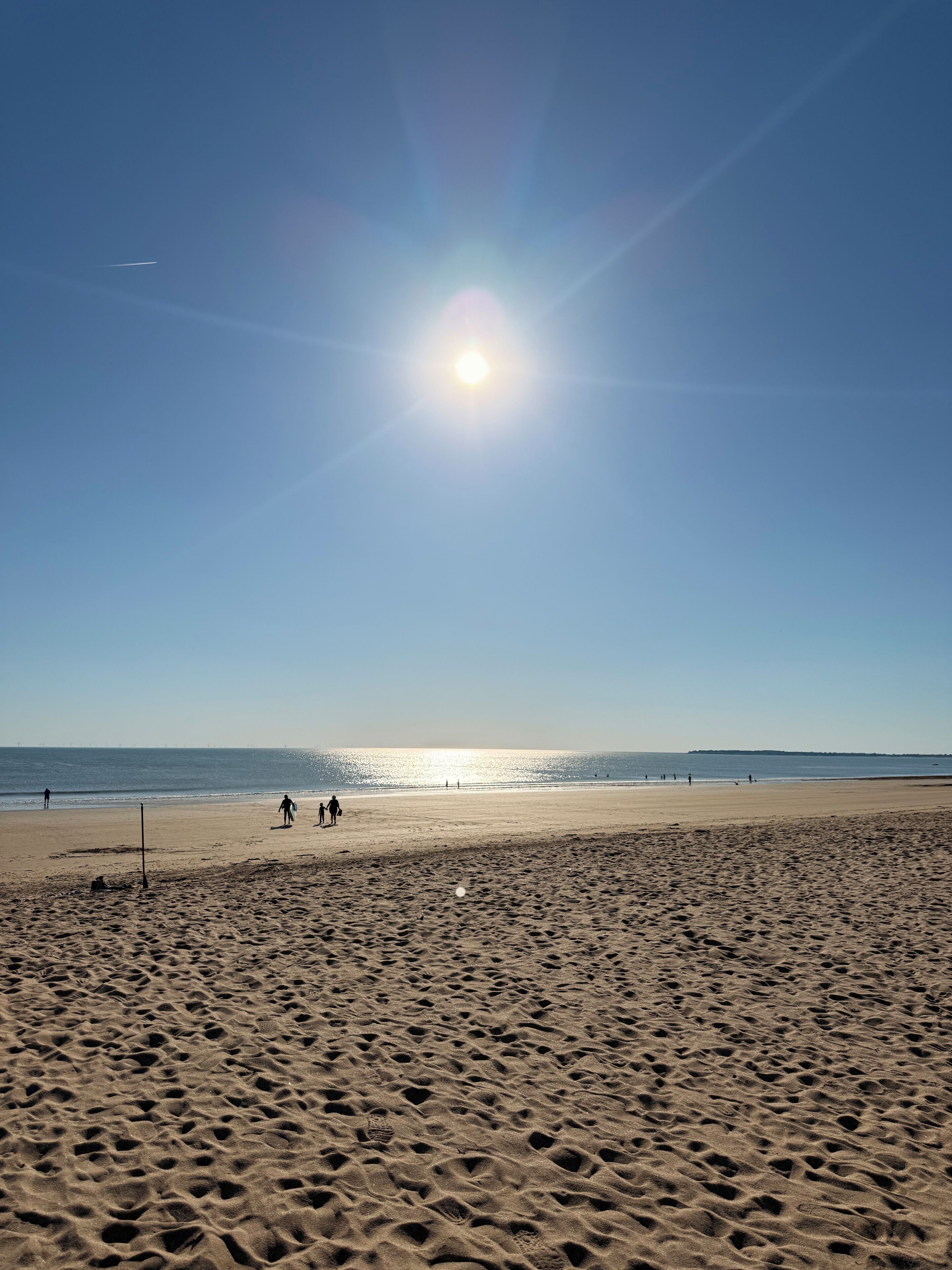 A beach with footprints in the sand, a clear sky, and the sun shining.