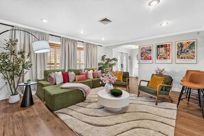 Ein modernes Wohnzimmer mit einem grünen Sofa, einem runden Couchtisch und einem großen Fenster mit Vorhängen.