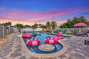 Ein Swimmingpool mit rosa Flamingo-Schwimmyolkern, einer versunkenen, runden Liegeinsel und Liegestühlen.