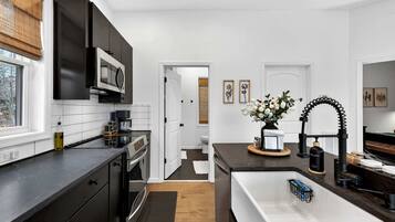 Une cuisine moderne avec des meubles de couleur sombre, un four à micro-ondes encastré et un îlot central doté d’un évier et d’objets décoratifs.