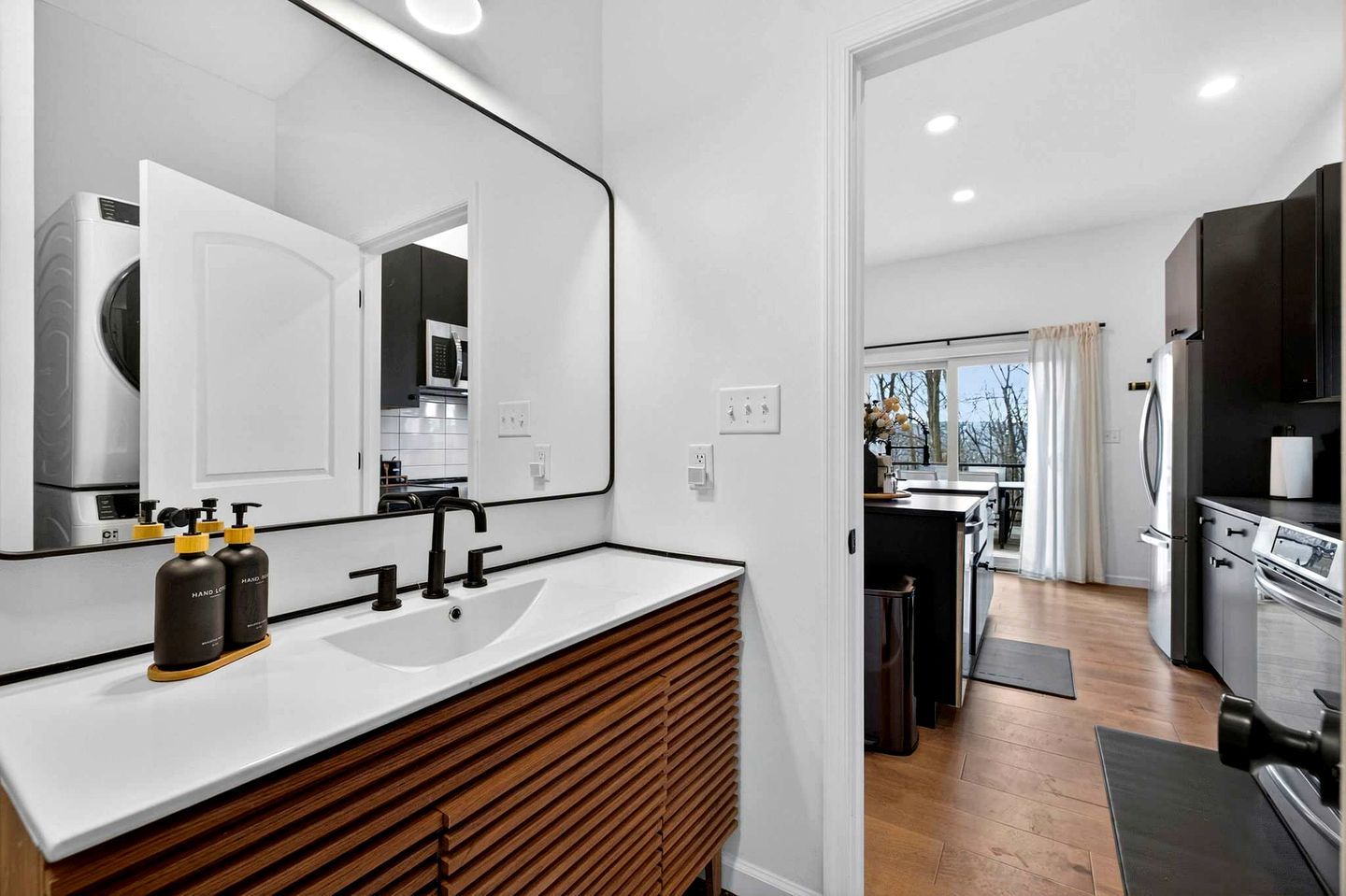 Une salle de bain moderne avec un grand miroir, un lavabo blanc et deux flacons de gel hydroalcoolique.