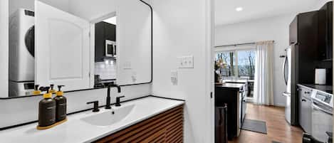 A modern bathroom with a large mirror, a white sink, and two hand sanitizer bottles.