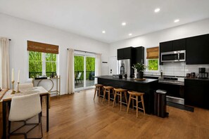 Una cocina moderna con una isla central, taburetes de bar y un comedor con mesa y sillas.