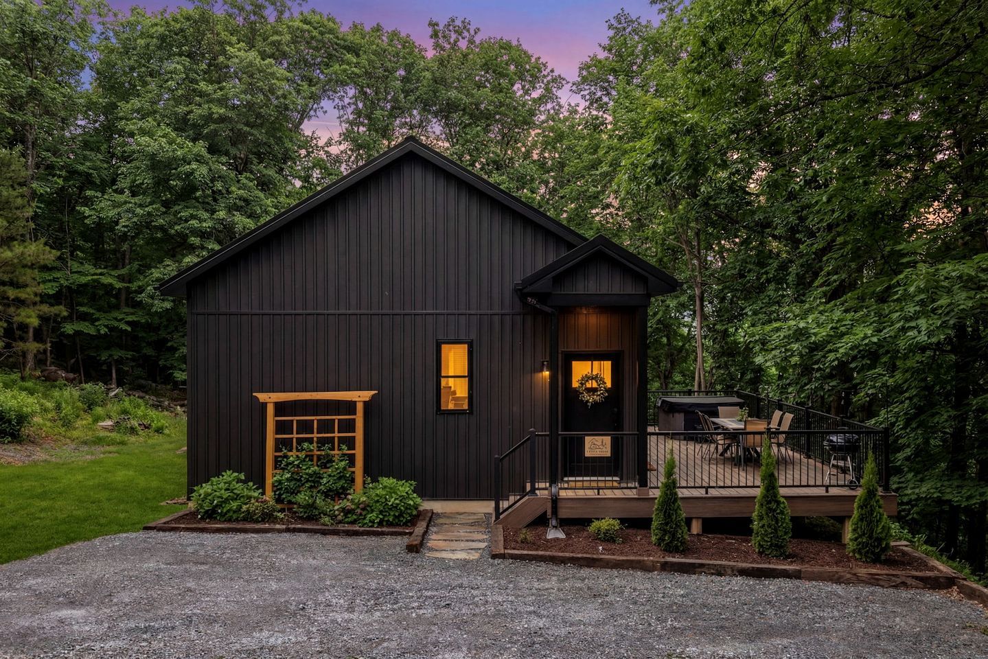 A dark-colored building with a front door, a small porch, and a gravel driveway.