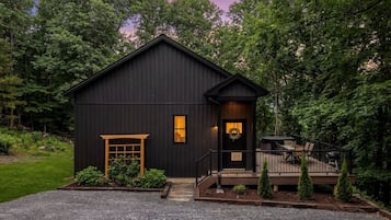 A dark-colored building with a front door, a small porch, and a gravel driveway.