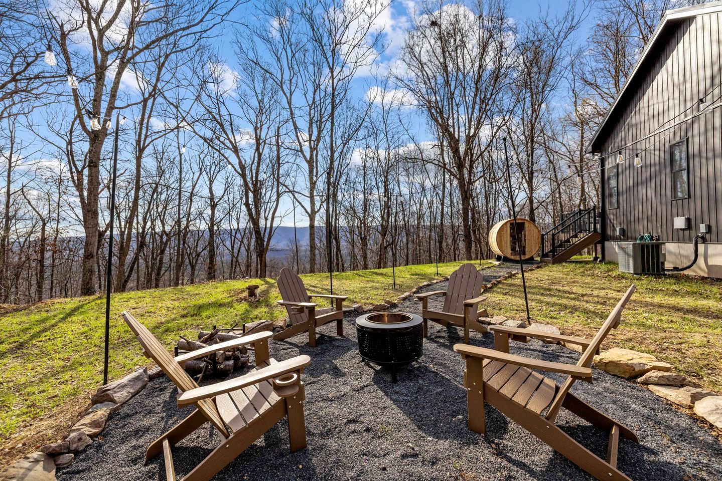 An outdoor seating area with Adirondack chairs and a fire pit, surrounded by trees and a building.
