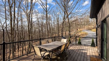 A wooden deck with a table and chairs, surrounded by trees, and a view of a road.