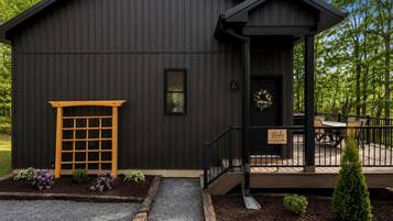 A black metal building with a wooden door, a small porch, and a gravel driveway.