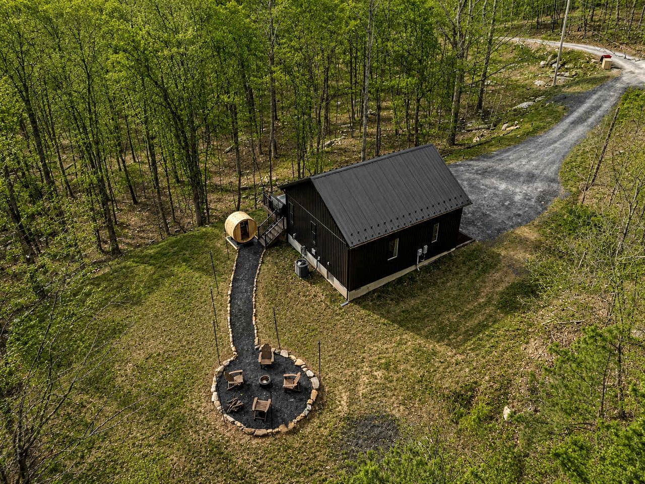 Une cabane dotée d’un espace extérieur circulaire aménagé en salon, entourée d’un paysage boisé.