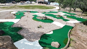 A miniature golf course with multiple holes, green artificial turf, and white pathways. - Stylish Tiny Home with Fire Pit & Stargazing Deck Near Fredericksburg, TX (Fredericksburg)