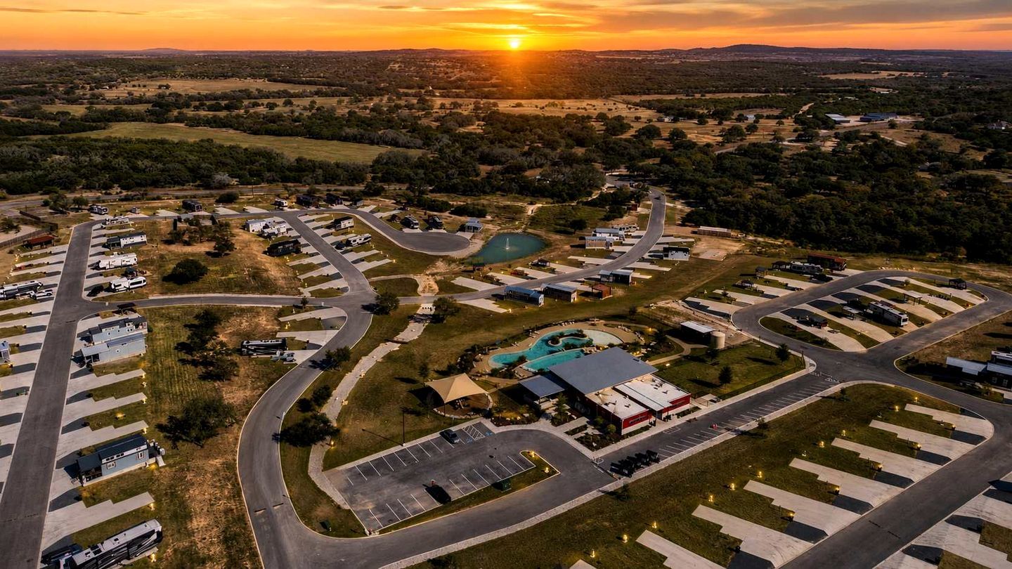 Ein Luftbild zeigt einen Campingplatz mit mehreren Stellplätzen für Wohnmobile, einem Schwimmbad und einem großen Gebäude mit rotem Dach.