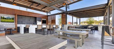 Un espace extérieur aménagé en terrasse, avec plusieurs coins salon, un barbecue et une cheminée en pierre.
