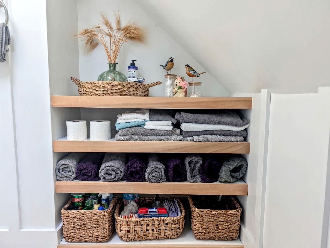Ein aufgeräumtes Badezimmer mit Regalen, auf denen Handtücher, Pflegeprodukte und dekorative Gegenstände Platz finden.