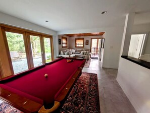 A pool table in a room with large windows, a sofa, and a view of the outdoors. - Coastal Beach House with Fireplace & Pool Table in Franklin, Maine (Franklin)