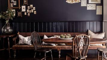 A dark-themed dining area with a wooden bench, chairs, a table with a plate of artichokes, and a wall adorned with framed pictures.