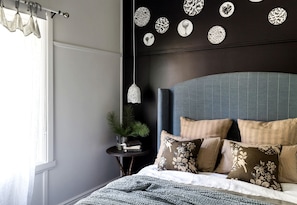 A bedroom with a bed, a nightstand, a potted plant, and wall decor.