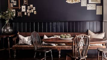 A dark-themed dining area with a wooden bench, chairs, a table with a plate of artichokes, and a wall adorned with framed pictures.