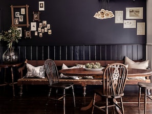 A dark-themed dining area with a wooden bench, chairs, a table with a plate of artichokes, and a wall adorned with framed pictures.
