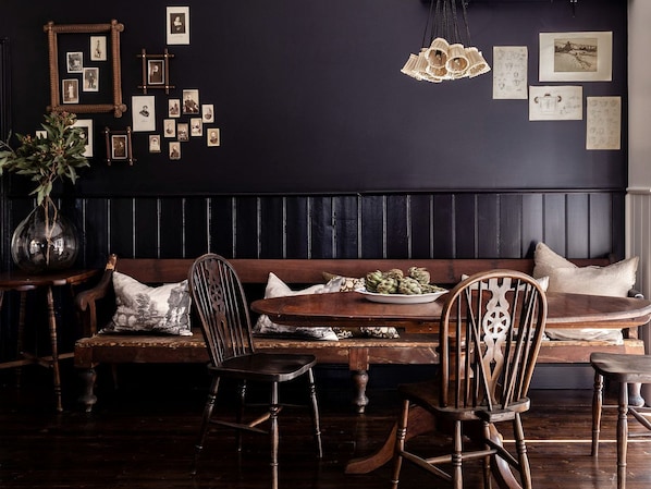 Un comedor de ambiente oscuro con un banco de madera, sillas, una mesa con un plato de alcachofas y una pared decorada con fotografías enmarcadas.