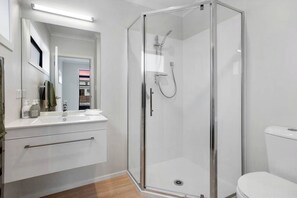 Un bagno moderno con box doccia in vetro, un lavandino bianco con specchio e un water.