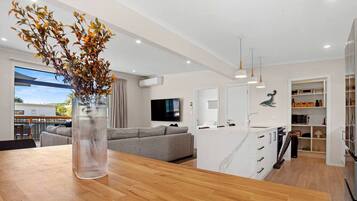 A modern kitchen with a central island, a dining area with a wooden table, a grey sofa, and a large window.