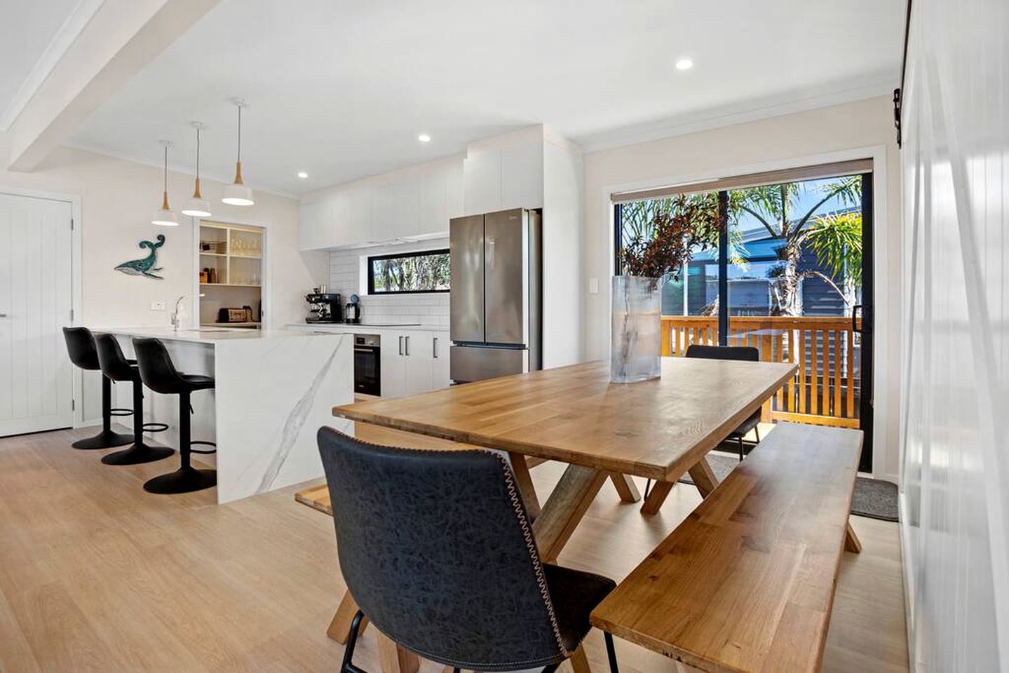 A modern kitchen with white cabinets, a wooden dining table, and bar stools.