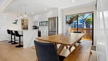 A modern kitchen with white cabinets, a wooden dining table, and bar stools.