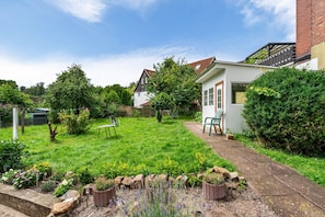 A well-maintained garden with a lawn, a small table and chairs, and a pathway leading to a white building with a door.