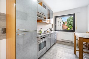 Une cuisine moderne avec des meubles gris, un four encastré et une fenêtre donnant sur un quartier résidentiel.