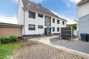 A two-story building with a tiled roof, a visible entrance, and a small outdoor seating area with chairs.