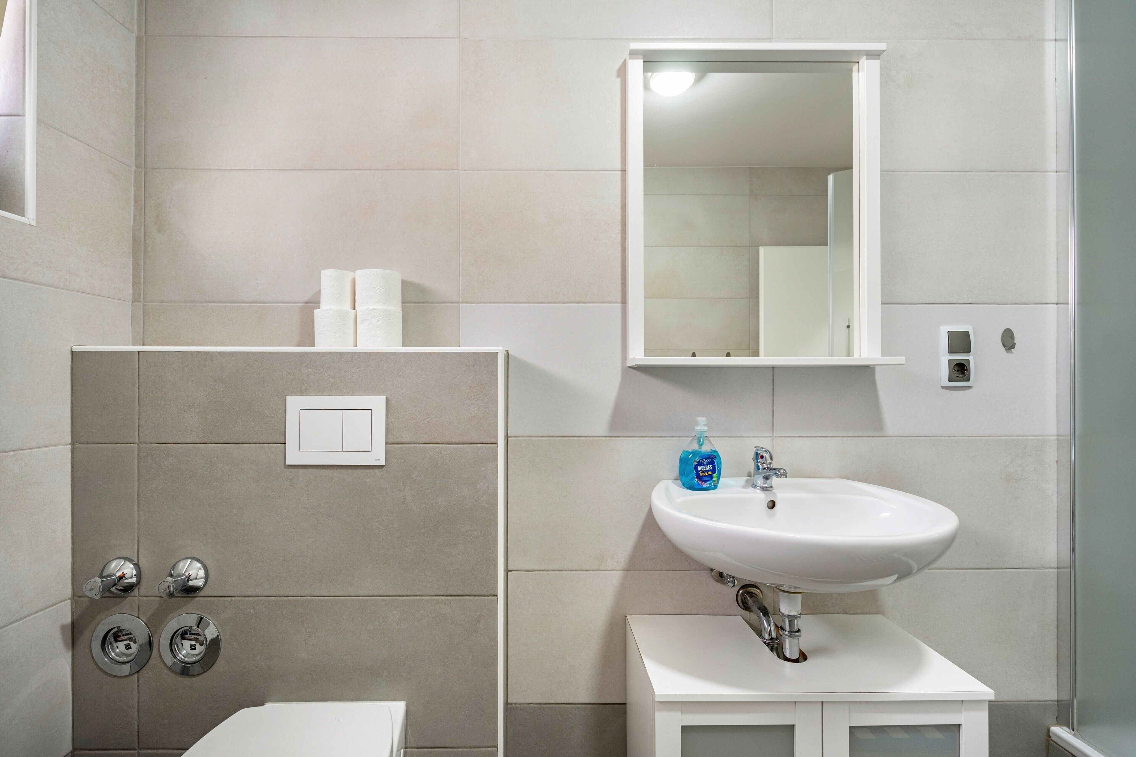 Ein Badezimmer mit einem weißen Waschbecken, einem Spiegel und zwei Toiletten.