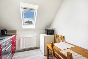 Una cocina compacta con ventana, microondas, tetera y una mesa con sillas.