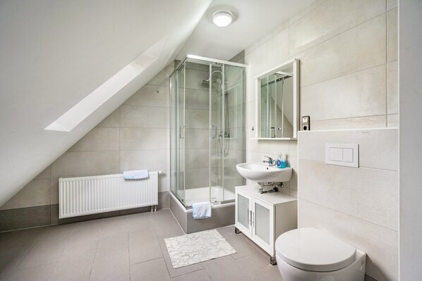 Un baño moderno con cabina de ducha de vidrio, un lavabo blanco y un inodoro.