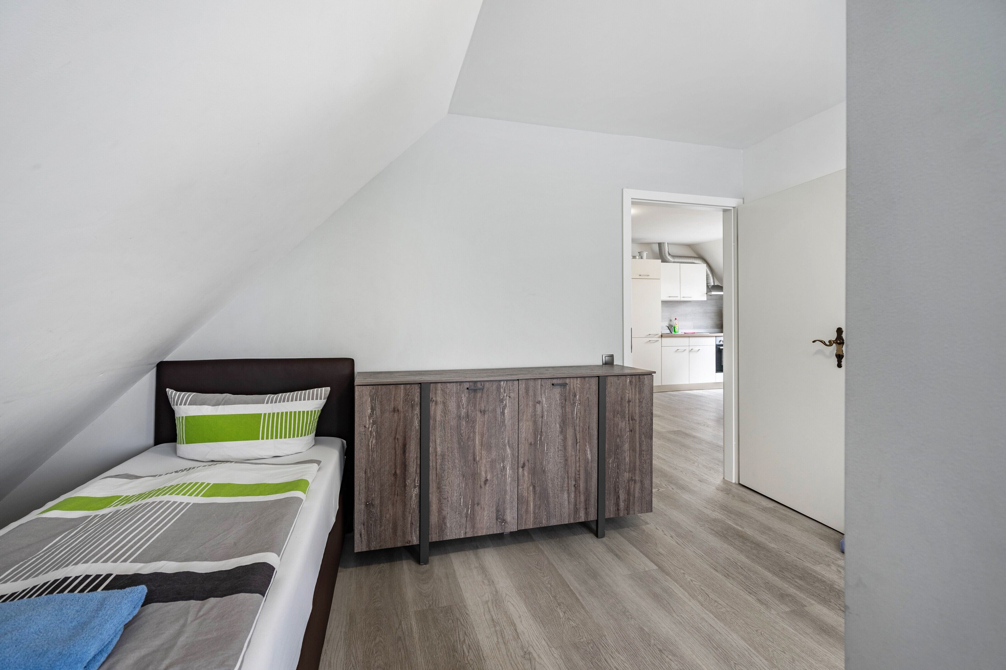 A bedroom with a sloped ceiling, a bed with patterned bedding, a bedside table, and a wardrobe.