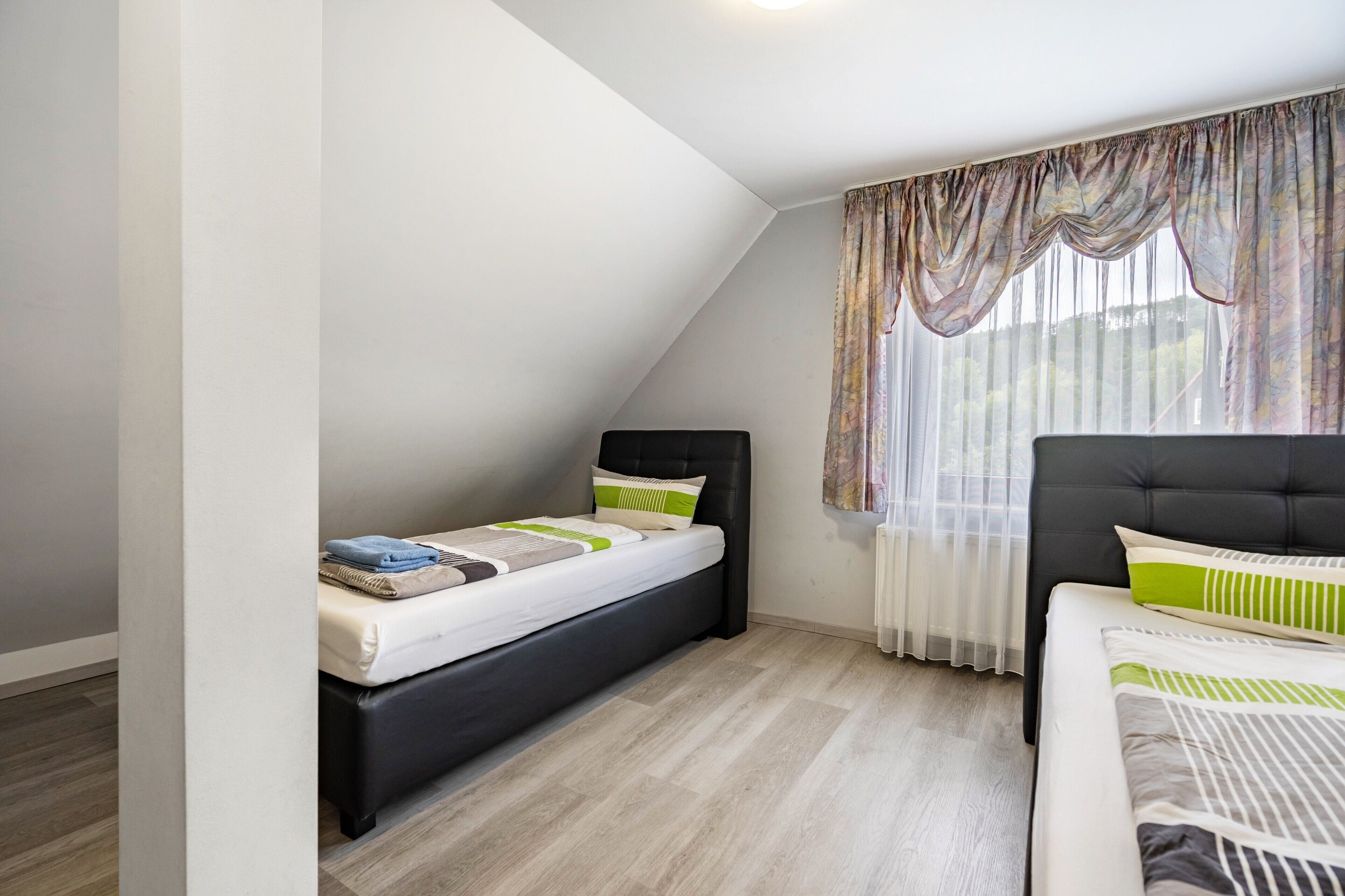Ein Schlafzimmer mit einem Bett, einem zusätzlichen Bett und einem Fenster mit Vorhängen.
