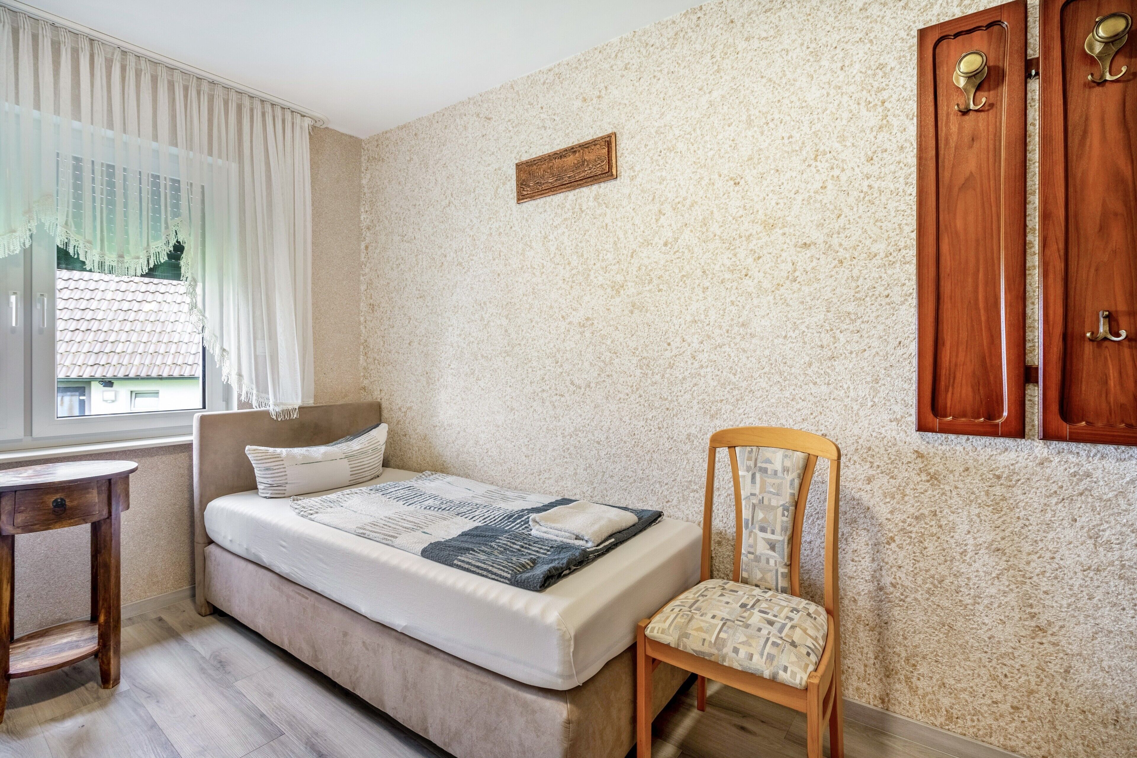 Ein Schlafzimmer mit einem Bett, einem Sessel, einem Schreibtisch und einem fenster mit Vorhängen.