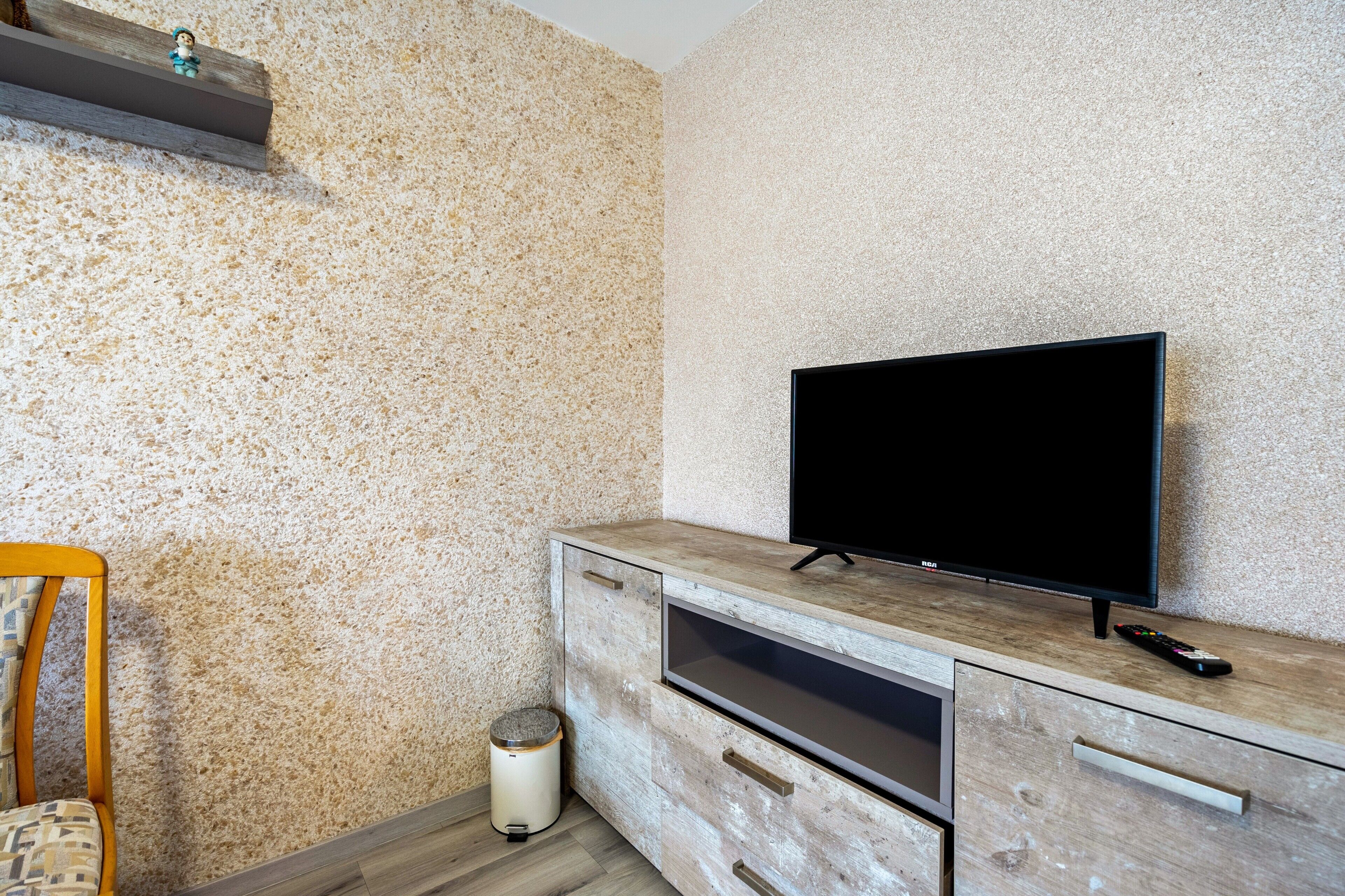A modern living room with a television on a wooden cabinet, a small trash bin, and a chair.