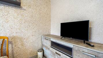 A modern living room with a television on a wooden cabinet, a small trash bin, and a chair.