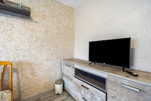 Una sala de estar moderna con un televisor sobre un mueble de madera, un cesto de basura pequeño y una silla.