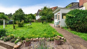 Un giardino residenziale con prato, un vialetto e un piccolo edificio bianco con porta e finestre.