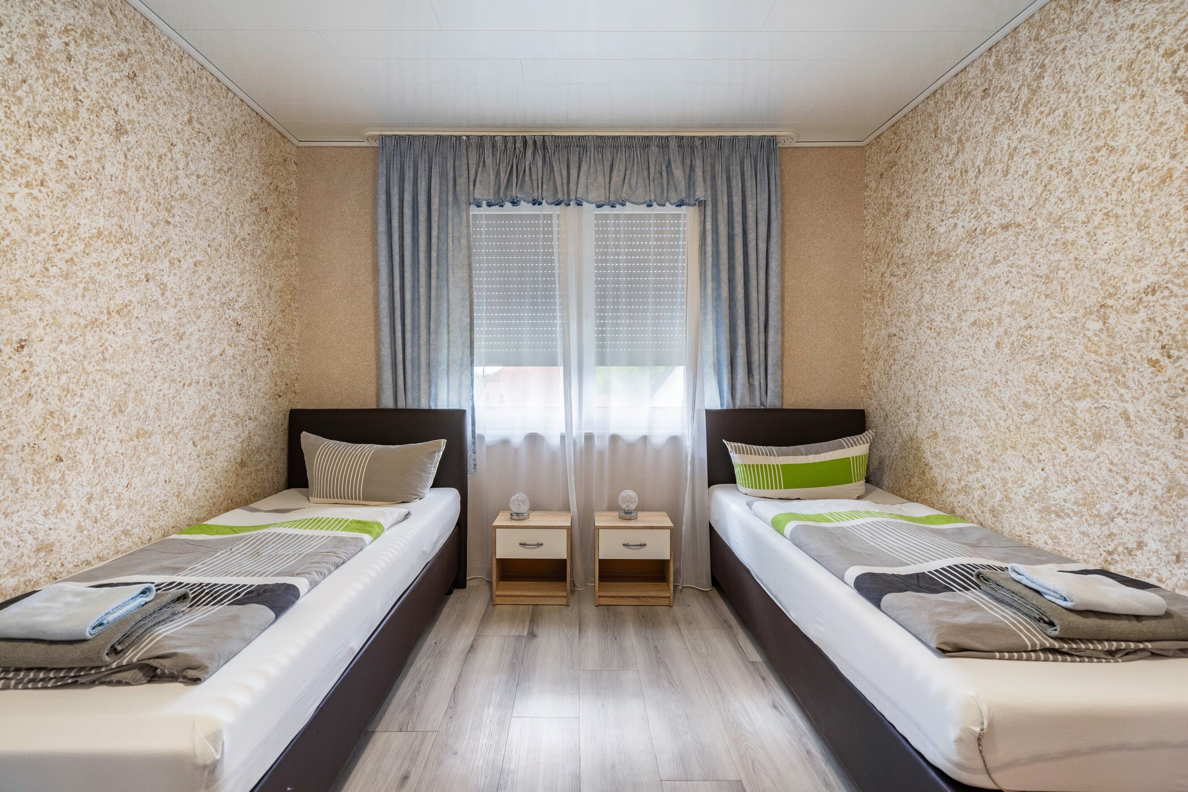 Ein Doppelzimmer mit zwei Betten, einem Fenster mit Vorhängen und Holzboden.