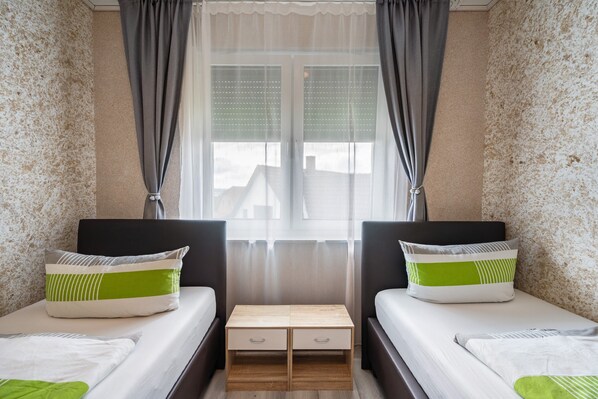 A bedroom with two beds, a nightstand, and a window with curtains.