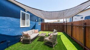Patio con un muro azul, cerca de madera, zona sombreada y mobiliario exterior.