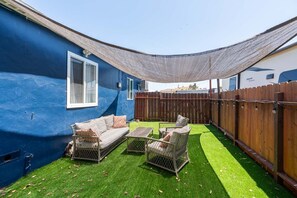 A backyard with a blue wall, a wooden fence, a shaded area, and outdoor furniture. - Entire 6BR Duplex Near Gaylord Resort (Chula Vista)